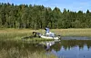 Amfibiemaskin på en innsjø foran skog og siv.