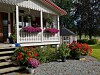 Hvit veranda med rosa og røde blomster foran et landlig hus.