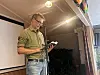 Mann med mikrofon og mobil står foran et lerret i et innendørslokale.