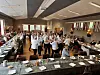 Mange gjester samles i en festpyntet sal rundt lange, dekkede bord.
