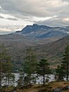 Fjell med innsjø og furutrær under en overskyet himmel.