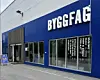 Blå Byggfag-butikk med store vinduer og inngang på gateplan.