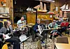 Musikkgruppe spiller med trekkspill, trommer, gitar og keyboard i et dekorert lokale.