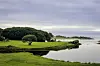 Frodige grønne marker og trær ved et stille vann/sjø under en overskyet himmel.