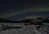 Snødekt gapahuk under grønne nordlys og stjernehimmel. Et stjerneskudd på himmelen.
