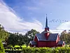 Rød kirke, kirkegård, busker og trær. Fugler på en lys himmel.