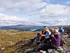 Turgåere sitter på steiner og tar kaffepause med utsikt over et vidstrakt fjellandskap.