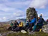 Turgåere sitter ved en steinvarde i et åpent fjellandskap.