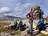 Fotturister tar pause ved en steinvarde i et steinete fjellandskap.