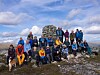Turgåere i fargerike klær står samlet ved en steinvarde på en fjelltopp.