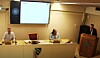 Taler ved talerstol foran et panelbord i et konferanserom.