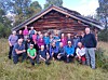 Gruppe mennesker poserer foran en tømmerhytte i et skogkledd område.