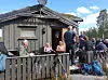 Mennesker samles foran et gammelt trehus med kamera- og annet utstyr i forgrunnen.
