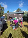 Gruppe turgåere med sekker utenfor en trehytte i solskinn.