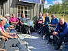 Eldre mennesker sitter sammen på en solrik treterrasse rundt et bord.