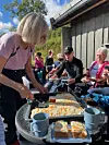 Kvinne serverer kake og kaffe ved et bord under en utendørs samling.