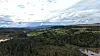 Panoramautsikt over skog, åkrer, vann og åser under en skyfylt himmel.