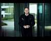 Smilende mann i svart antrekk står foran glassvegger i en moderne bygning.