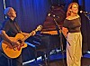 Gitarist og kvinnelig vokalist opptrer ved et flygel på en scene.