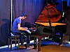 Pianist spiller på et flygel på en mørklagt scene.