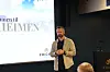 Foredragsholder på scenen foran en presentasjonsskjerm med tekst.