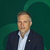 Mann i mørk dressjakke foran en grønn bakgrunn med buemotiv.