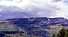 Vidstrakt fjellandskap med snøflekker, vegetasjon og tunge skyer.