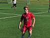 Fotballspiller i rød drakt på en grønn kunstgressbane under kamp.