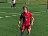 Fotballspiller i rød drakt på en grønn kunstgressbane under kamp.