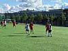Ungdommer i fotballdrakter spiller på en kunstgressbane foran en skolebygning.