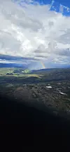 Regnbue over skog, innsjøer og jordbrukslandskap under store skyer.