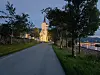 Opplyst kirke ved en vei, med trær og sjøen i bakgrunnen under blå skumring.