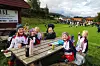 Smilende jenter i treningstøy sitter rundt et trebord på en grønn plen.