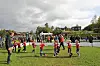 Barn spiller fotball på en gressbane med tilskuere langs sidelinjen.