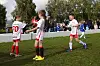 Tre unge fotballspillere i hvite og røde drakter på gressbanen.