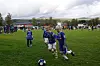 Unge fotballspillere løper etter ballen på en gressbane med publikum og fjell i bakgrunnen.