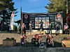 Flere motorsykler står foran en scene med sponsorplakater under et utendørs arrangement.
