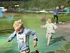 To barn løper gjennom farget pulver på en grønn utendørsarena.