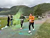 Løpere passerer gjennom farget pulver på en grussti omgitt av grønne fjell.