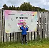 Ung deltaker i blå jakke foran banneret til Vi bryr oss-løpet ved et tregjerde.