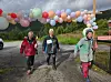 Tre turgåere går på en våt vei under fargerike ballonger.