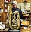 Mann holder en stor messingtuba i et trepanelkledd interiør.