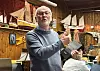 Mann med briller holder en modellbåt i et rom fylt med maritime modeller.