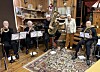 Blåseensemble med trompeter, tuba og trombone spiller rundt notestativer.