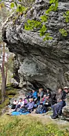 En gruppe turgåere sitter under et stort fjelloverheng i en skog.