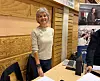 Kvinne ved en trevegg og utstillingsbord med datamaskin, nettbrett og plakater.