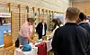 Besøkende og utstillere samles rundt en messebod i en idrettshall.