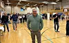 Mennesker samlet i en idrettshall, med en mann i grønn genser i forgrunnen.