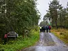 Gruppe turgåere på en våt grusvei i skogen, med skilt og høye trær rundt.