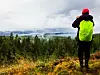 Turgåer med neongrønn jakke ser ut over skog og vann fra en høyde.